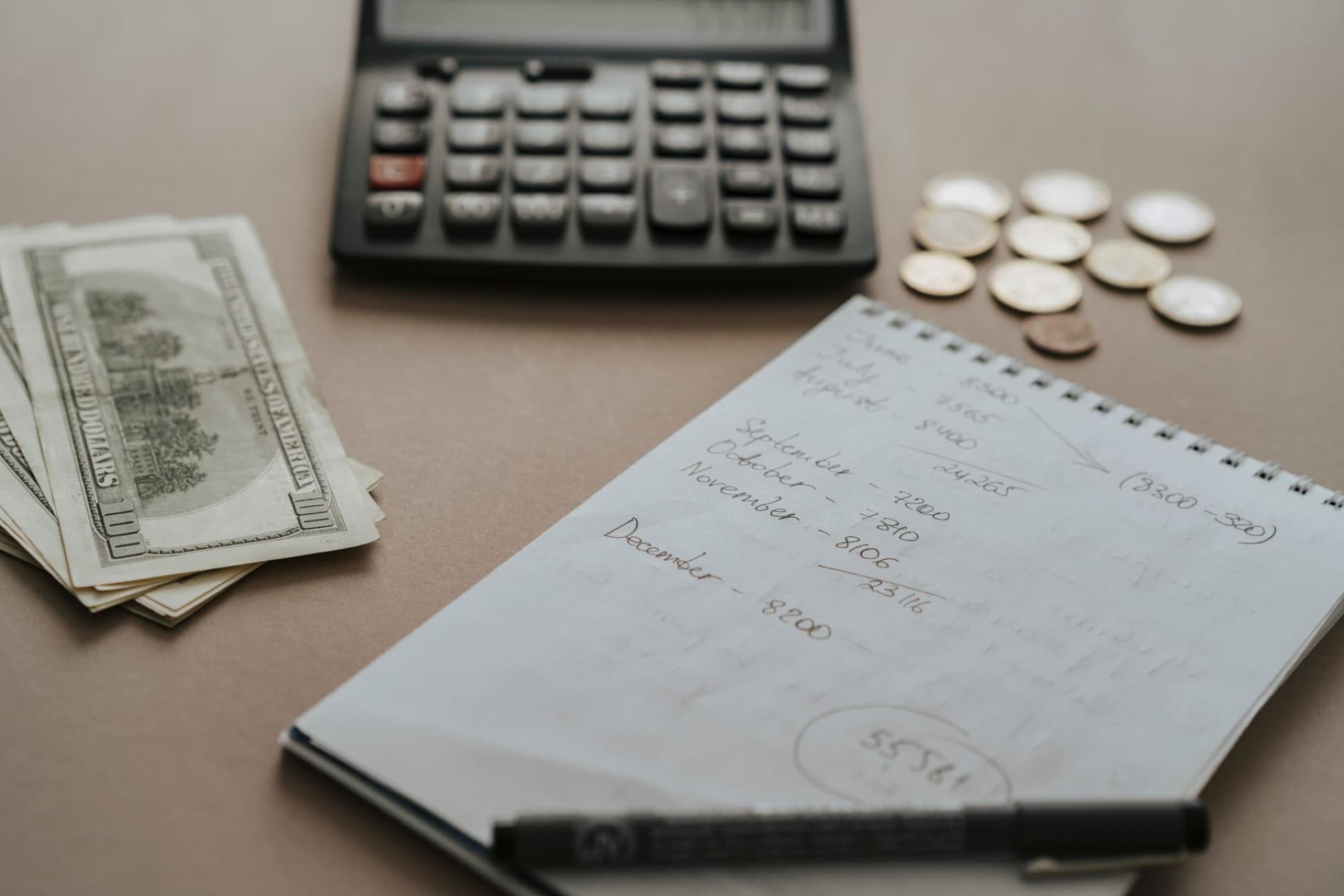 A calculator, notebook, and pen on a kitchen table